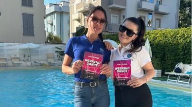 Two women pose with flyers for a poolside party.