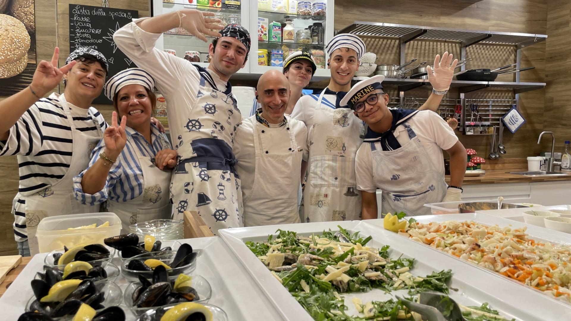 Gruppo di cuochi sorridenti in cucina con piatti di cozze e insalata.