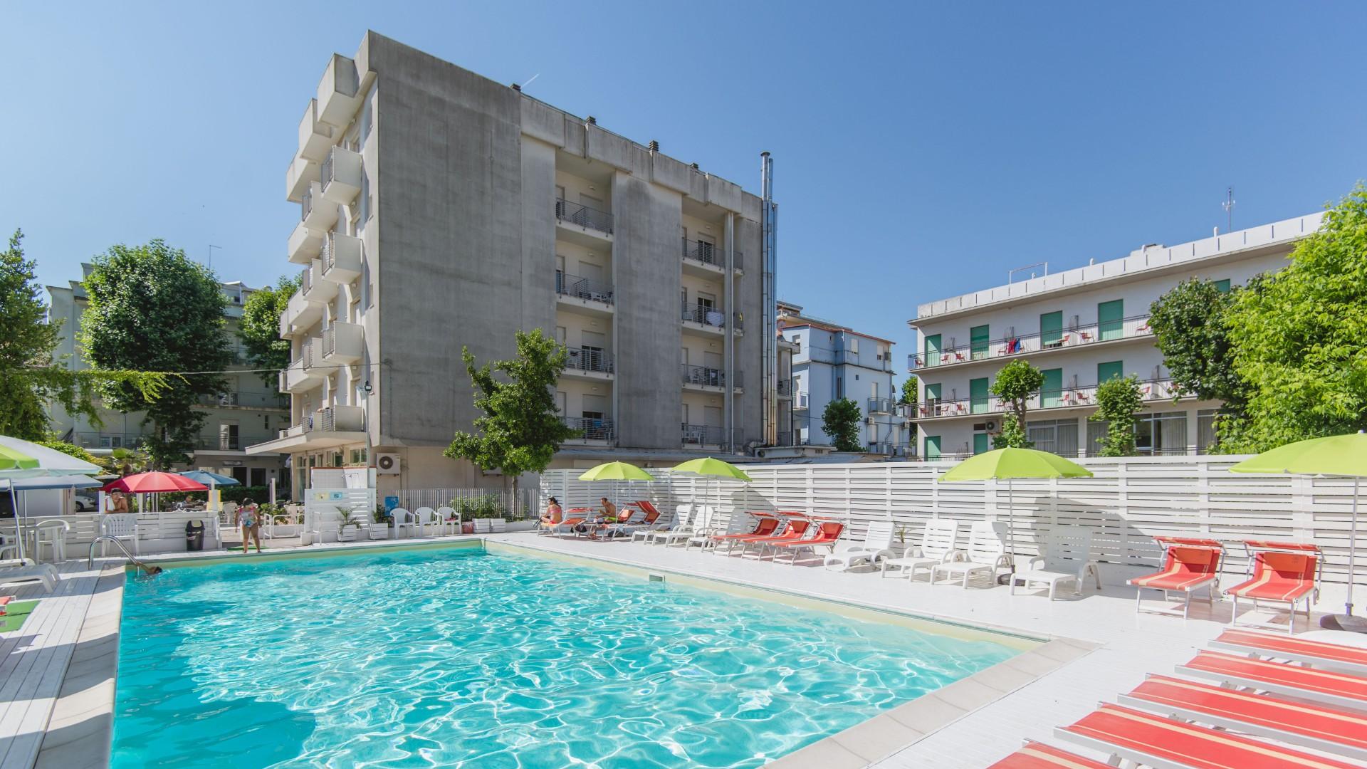 Piscina all'aperto con lettini e ombrelloni, circondata da edifici residenziali.