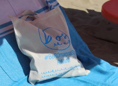 Borsa sulla spiaggia con hashtag #BeRomagnaStyle, Rimini, su asciugamano blu.