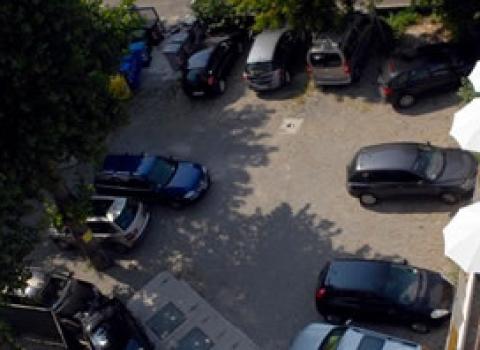 Parcheggio con auto e ombrelloni bianchi accanto a una piscina.