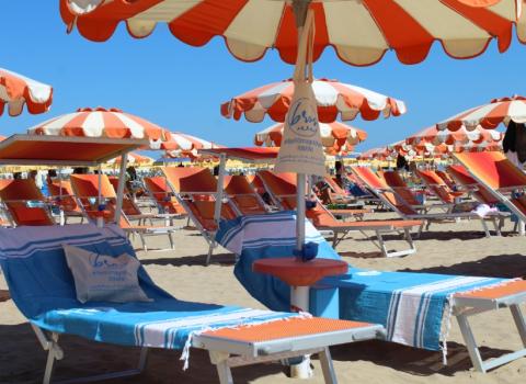 Spiaggia affollata con file di ombrelloni colorati e persone che si rilassano.