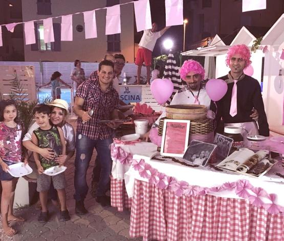 Festa a tema rosa con stand dolci e persone sorridenti in festa.