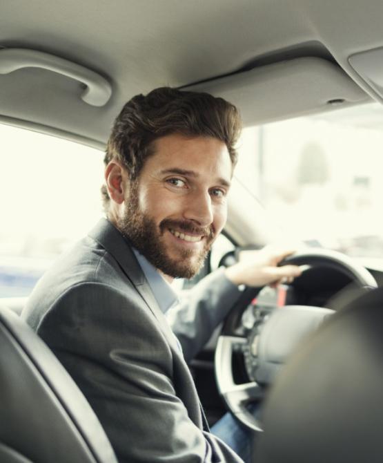 Uomo sorridente alla guida di un'auto, vestito in modo elegante.