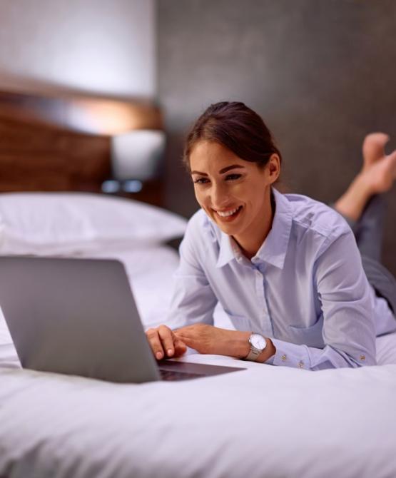 Donna sorridente lavora al computer portatile sdraiata sul letto.