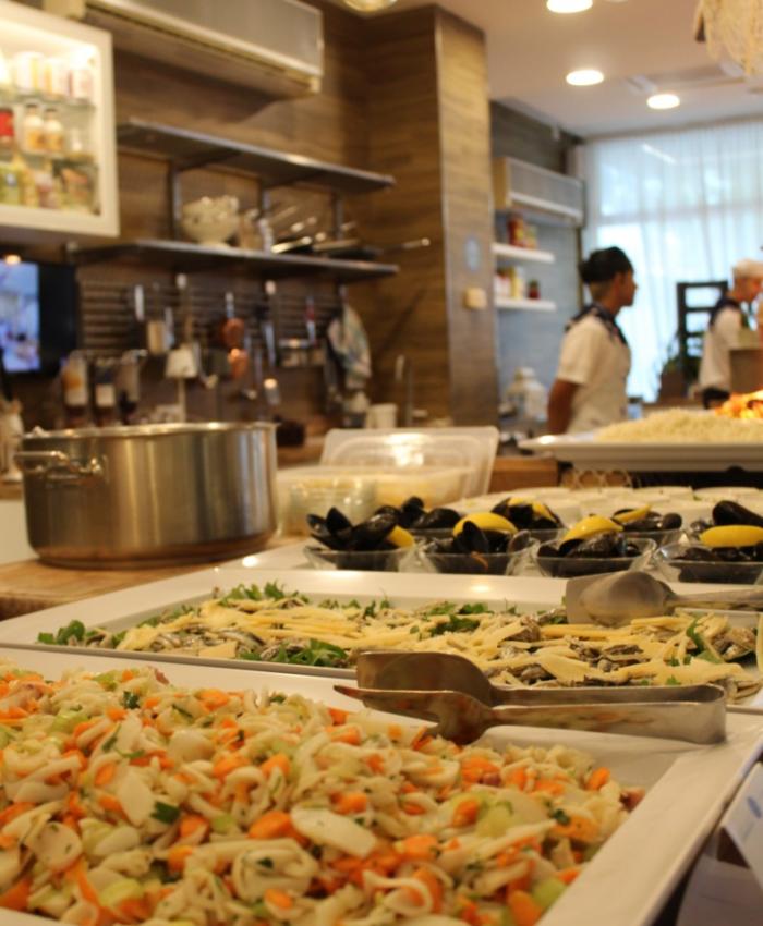 Cucina con piatti di pasta e frutti di mare, chef al lavoro sullo sfondo.