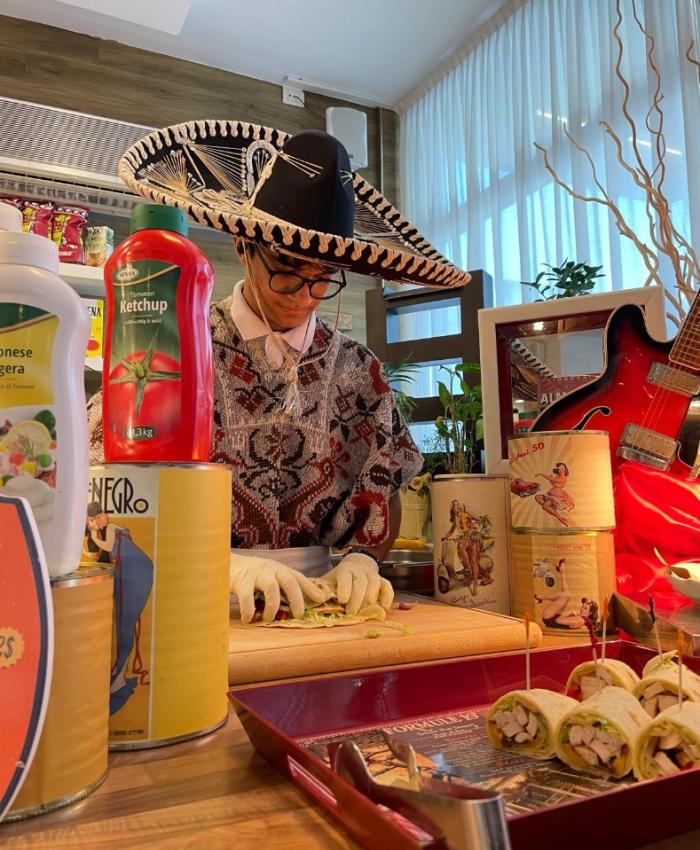 Persona con sombrero prepara cibo in un ambiente decorato con oggetti vintage.