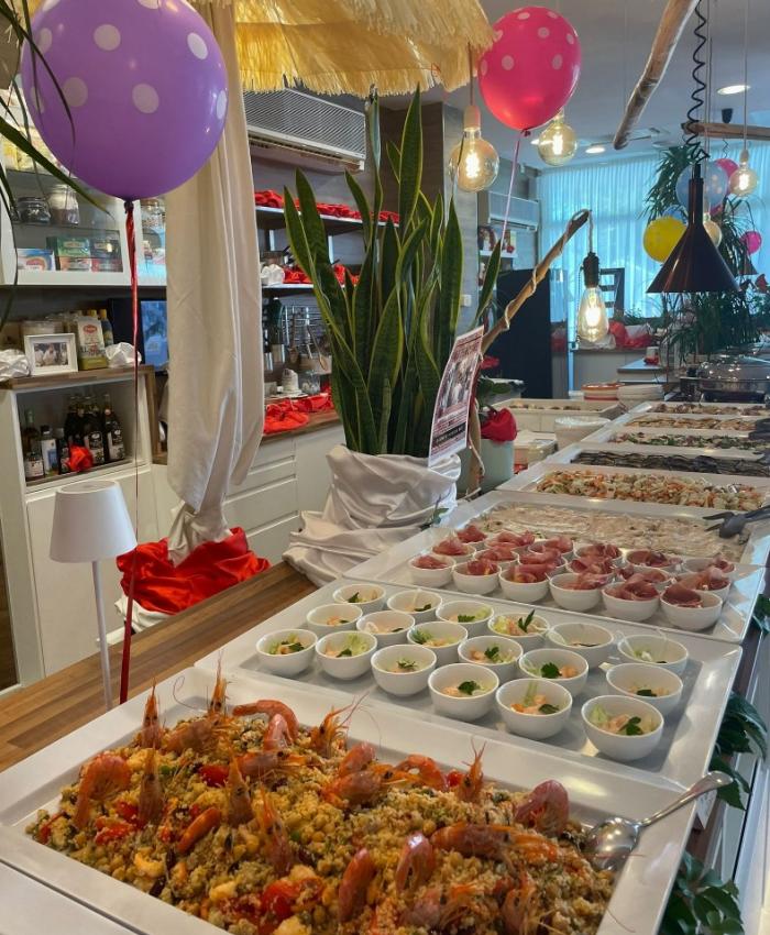 Buffet con piatti di pesce e decorazioni colorate, palloncini e atmosfera festosa.