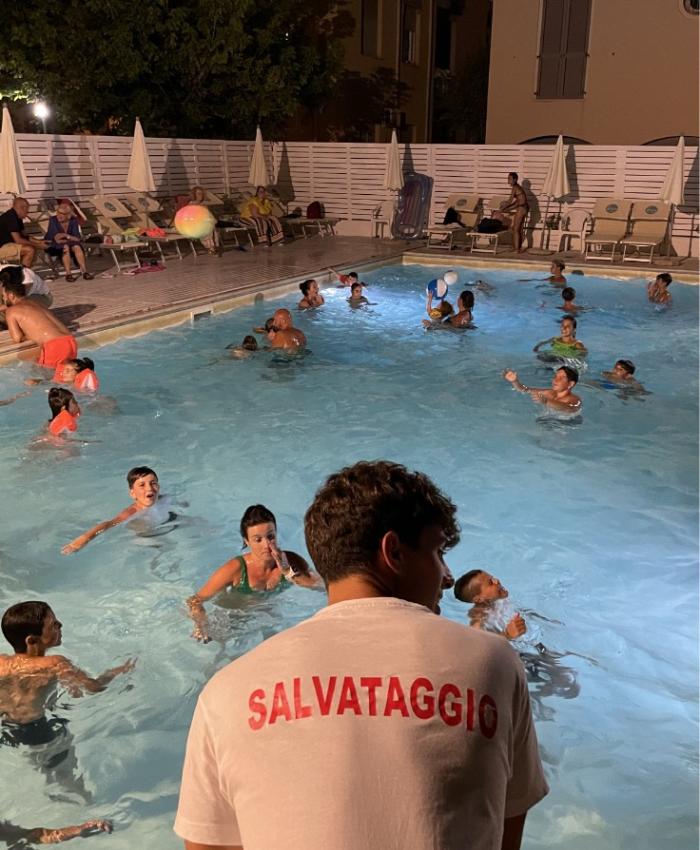 Piscina notturna affollata, bagnino vigila sulla sicurezza dei nuotatori.