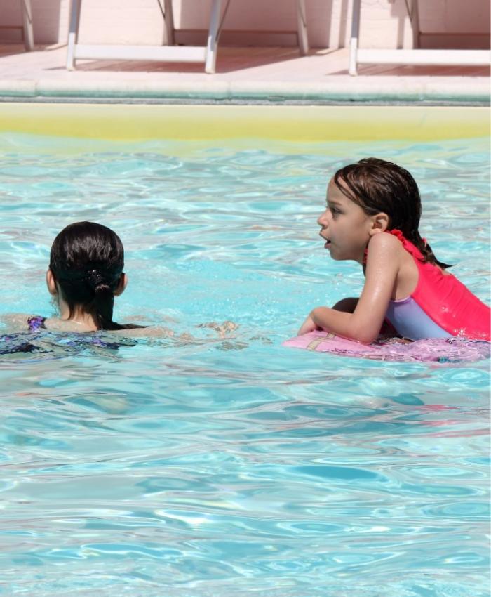 Due bambine nuotano in piscina, una con una tavoletta rosa.